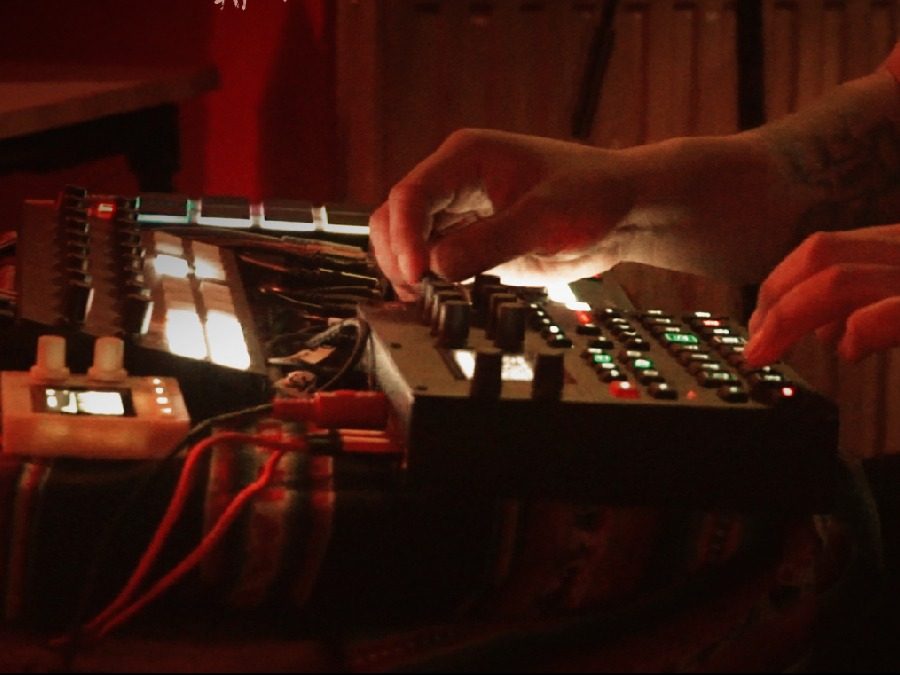 Hands on a synthesiser and sequencer in red light