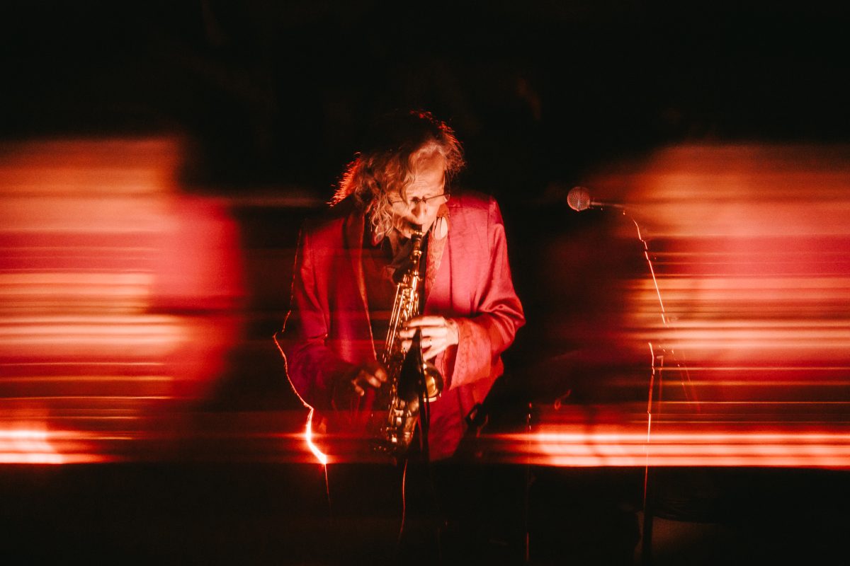 A saxophonist in a red jacket, blurred in streaks of red stage light
