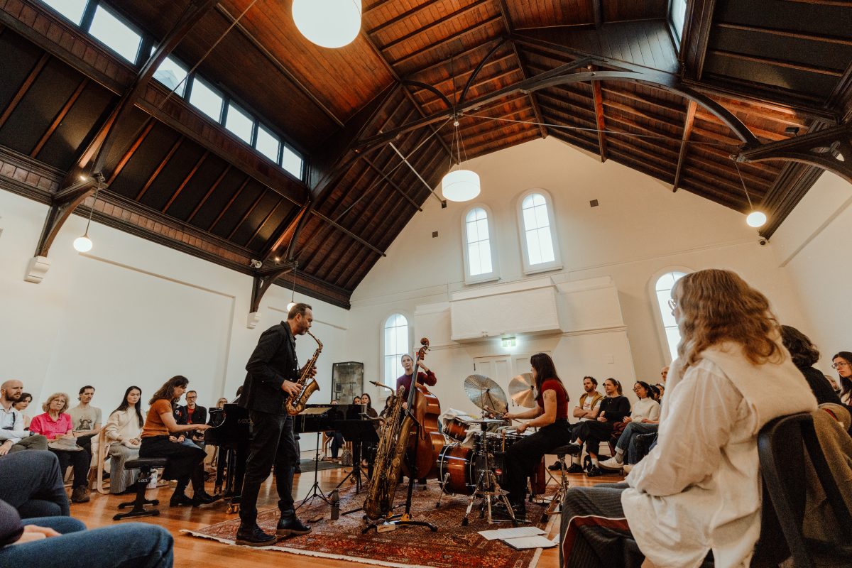 A quartet plays in a church hall with a steep timber roof and arched windows, watched by a seated audience