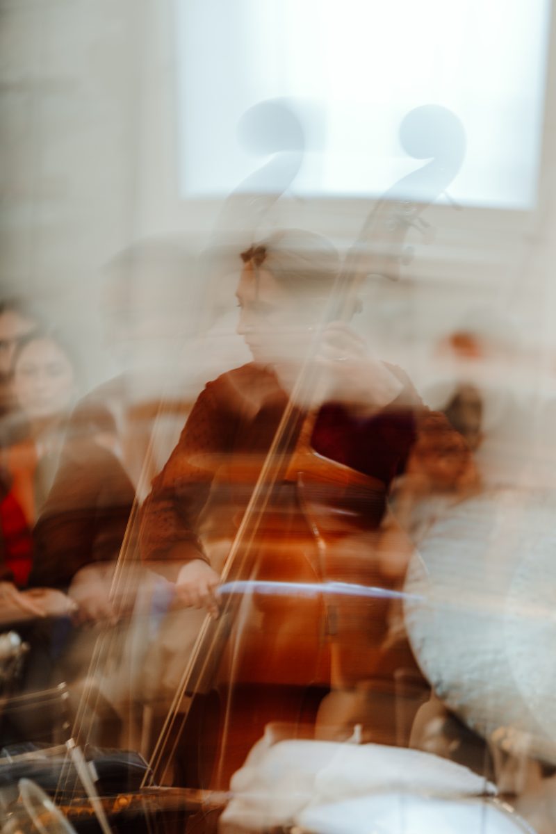 A double bass player seen through a soft long-exposure blur, with ghosted scrolls of the bass above