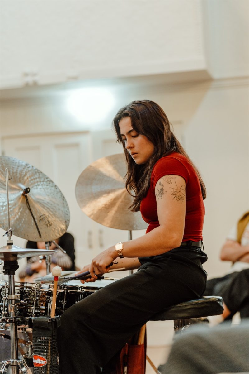 Drummer in a red top at the kit, cymbals behind her
